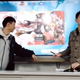 A Genshin Impact player stands with his professor in front of a projector screen with a Hu Tao banner up.